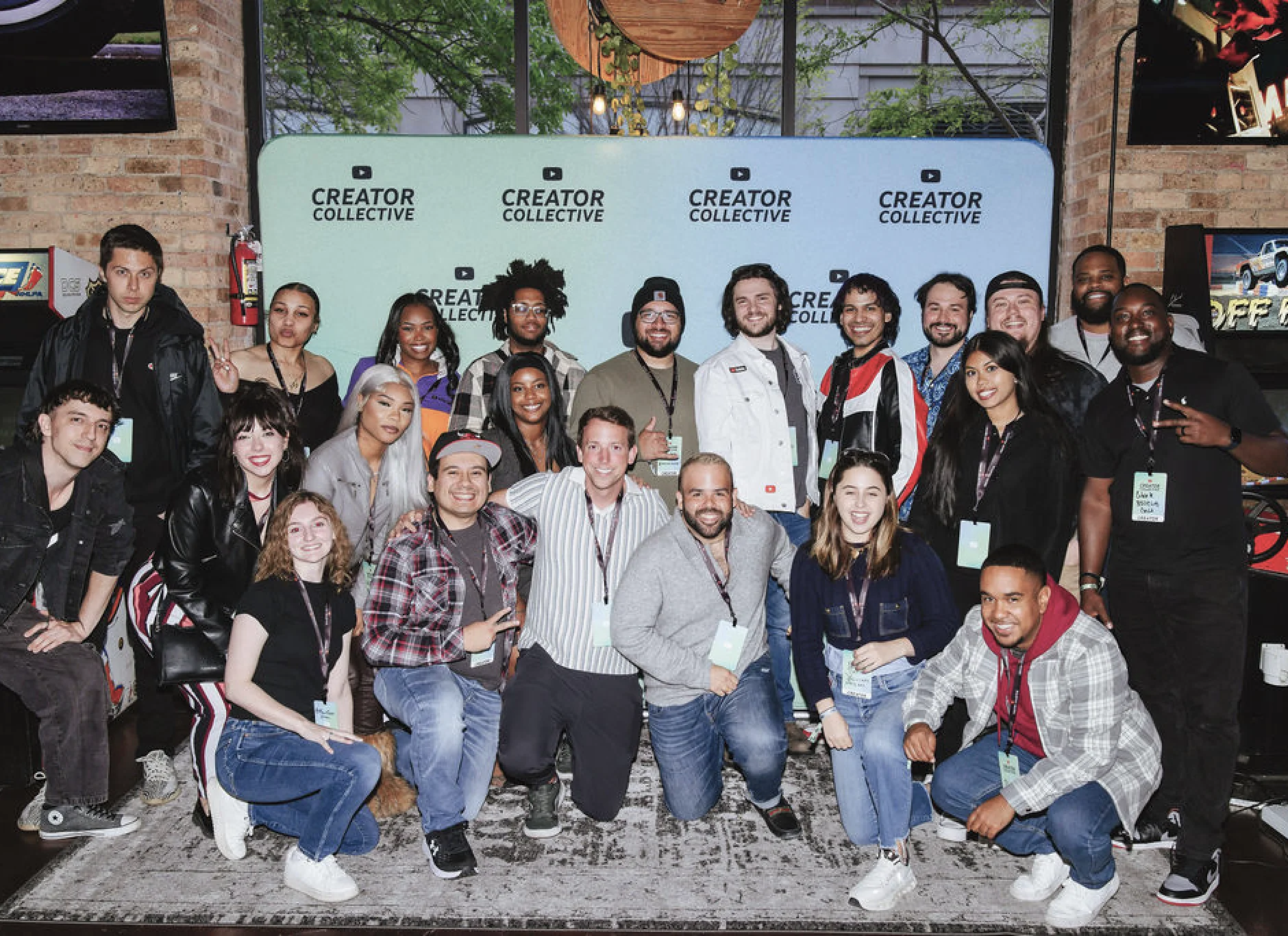 A group of people pose together indoors in front of a “Creator Collective” banner, smiling at the camera. Some wear lanyards and badges.