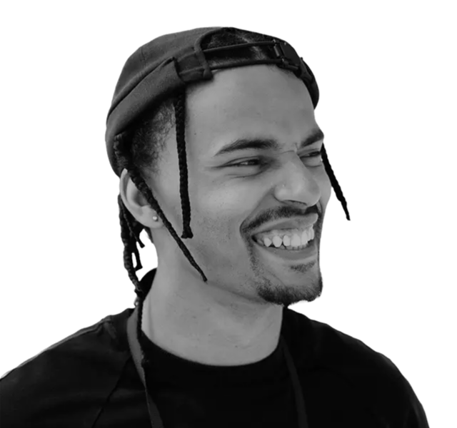 Man wearing a backward black cap and a dark shirt, smiling and looking to the side against a plain white background.