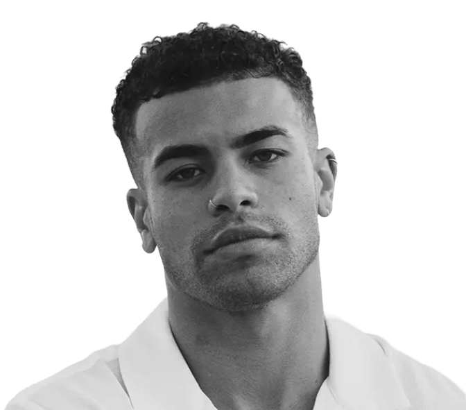 Black and white portrait of a man with short curly hair and a neutral expression, wearing a light-colored collared shirt, facing the camera against a plain background.