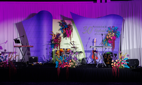 A decorated stage with musical instruments, colorful flower arrangements, and a backdrop reading "30th Essence Festival of Culture.